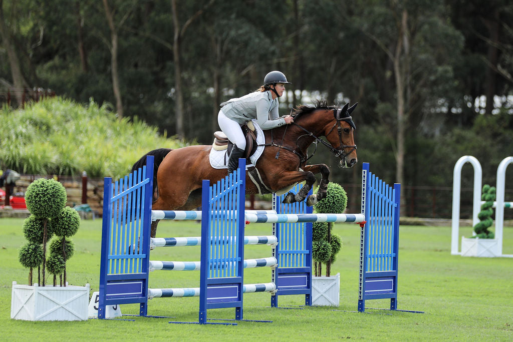 Rider competing in Wilma Sport Aero Competition Jacket in Platinum while showjumping over blue fence