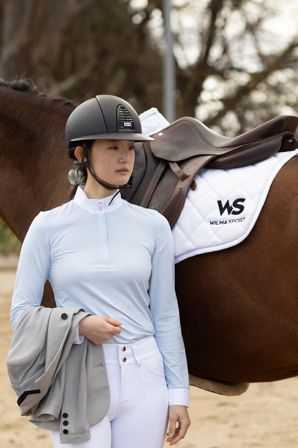 Model wearing Wilma Sport Featherlight Competition Shirt in Misty Blue standing beside a horse.