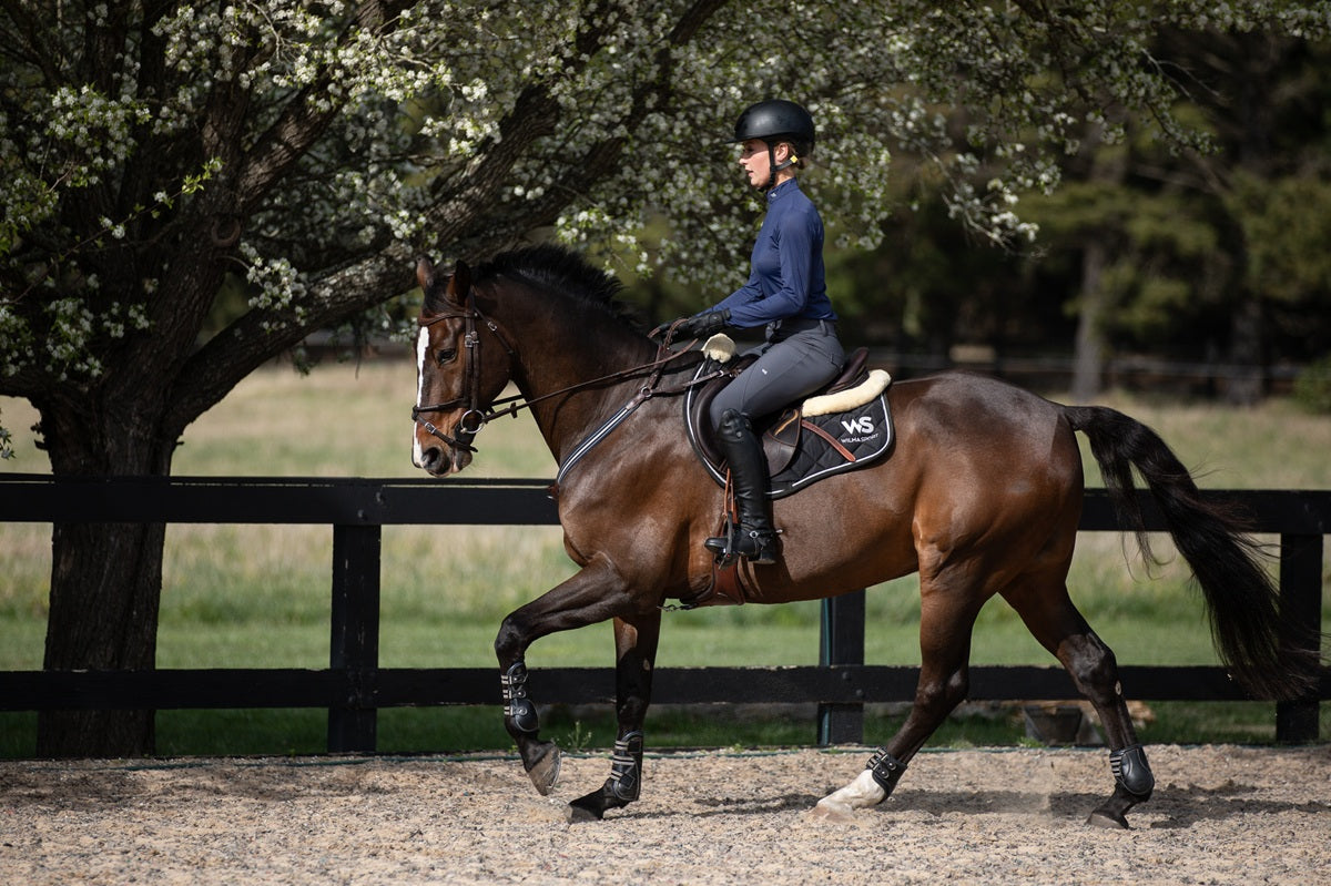 Model riding in Wilma Sport Slate Grey Hybrid Breeches – silicone knee grip breeches and Featherlight Training Shirt in Urban Navy.
